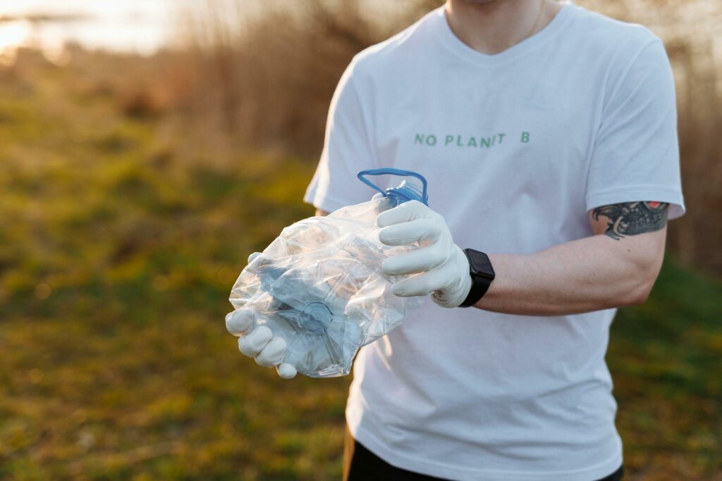 Adult man in a white shirt collecting plastic bottles in the countryside, promoting environmental awareness.