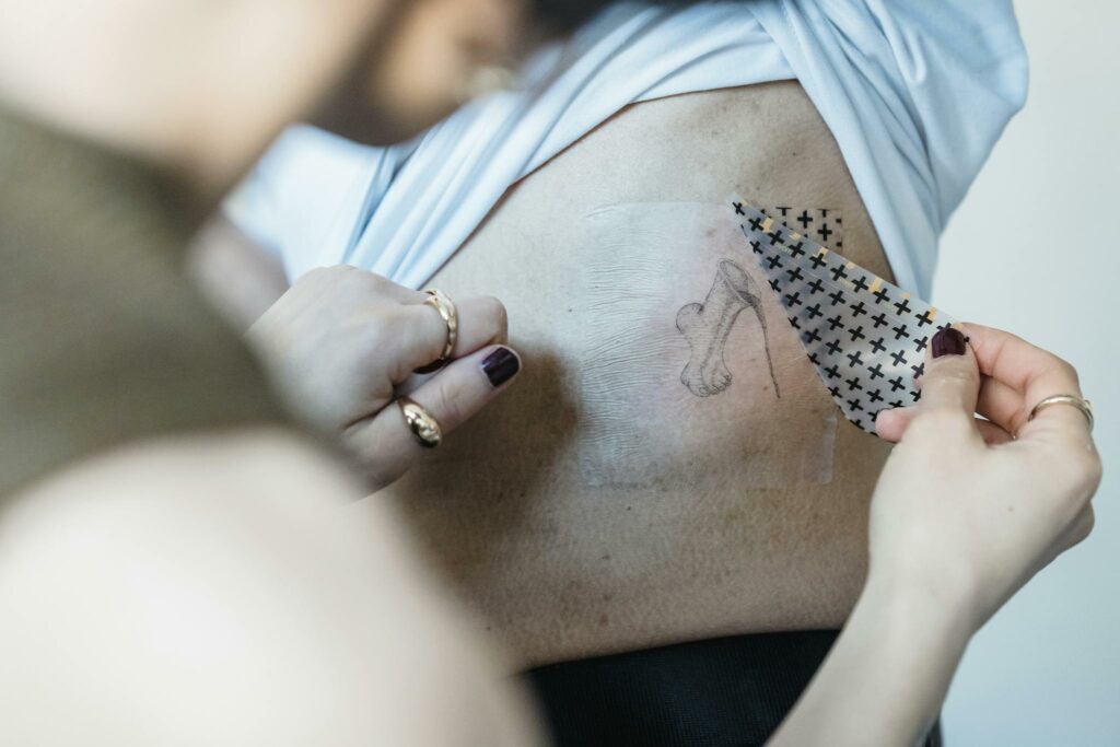 Detailed shot of a woman applying a temporary tattoo, showcasing rings and dark nail polish.